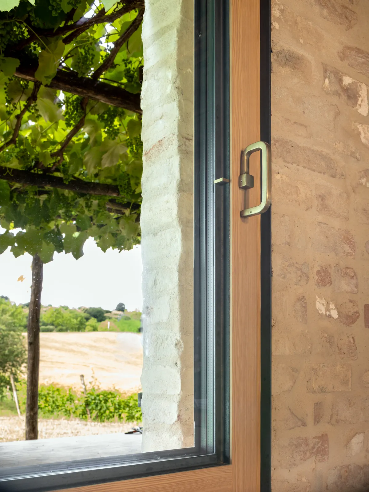 Finestra in larice spazzolato con maniglia in ottone e cornice in ferro, vista sui vigneti